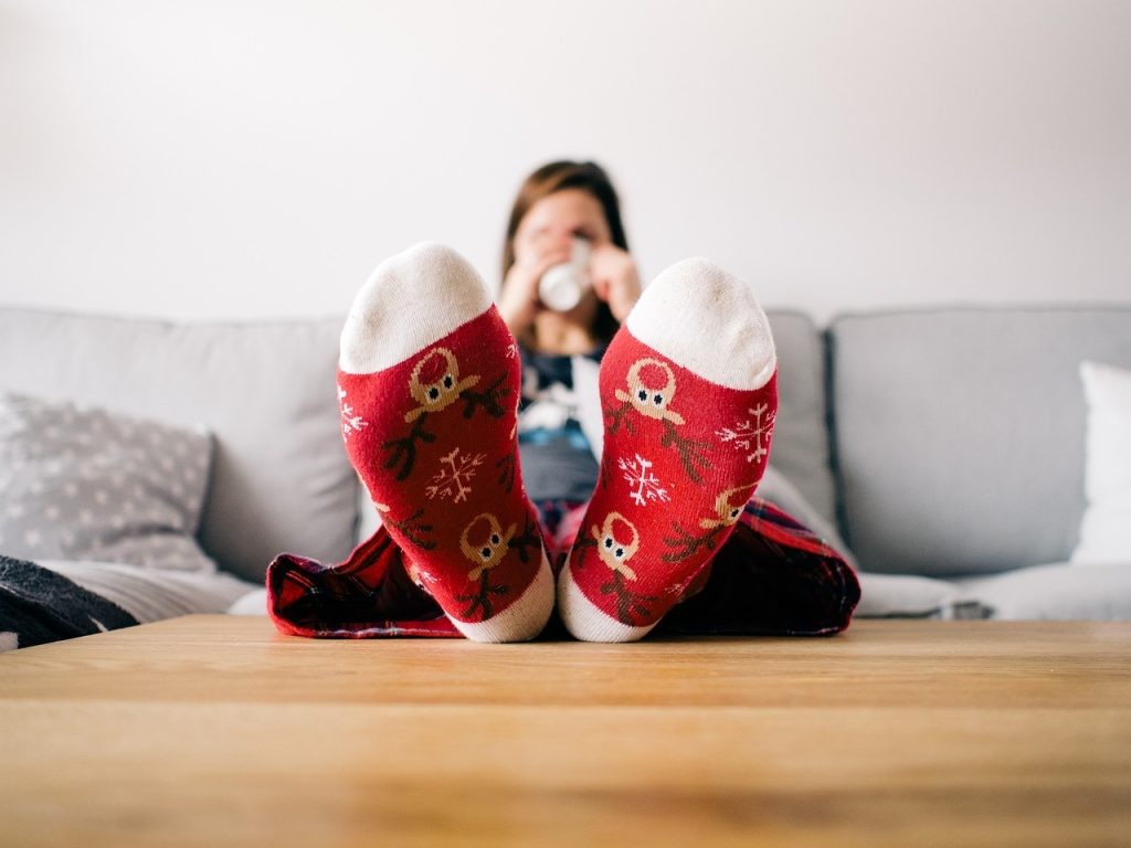 Femme assise sur un canapé buvant un café avec des chaussettes rouges, illustrant la procrastination à arrêter et la flemme à vaincre au quotidien pour être productif