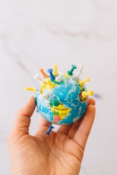 Main tenant un globe avec des épingles colorées pour illustrer la diversité des expériences de la périménopause à travers le monde.